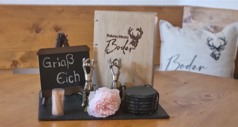 Een decoratieve tafel met een kleine tafel, een houten menu en verschillende accessoires. Op de achtergrond is een kussen met een hert-motief te zien.
