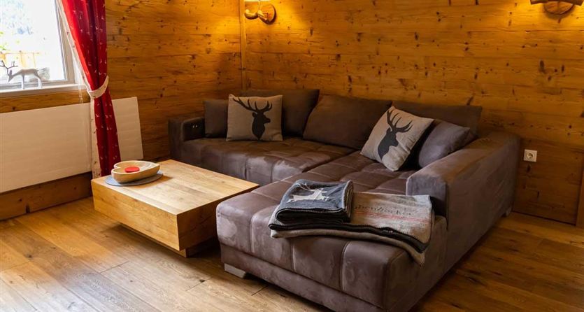 A cozy living room with a brown sofa and cushions. The wooden floor and walls give the room a warm atmosphere.