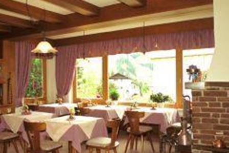 Una sala da pranzo accogliente con soffitto in legno e grandi finestre. I tavoli sono imbanditi con tovaglie viola e c'è un camino aperto.