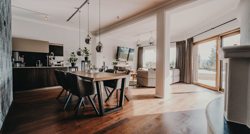 Ein modernes Wohn- und Esszimmer mit Holzboden und großen Fenstern. Der Raum ist hell und einladend, mit einem Esstisch und gemütlichen Sitzbereichen.