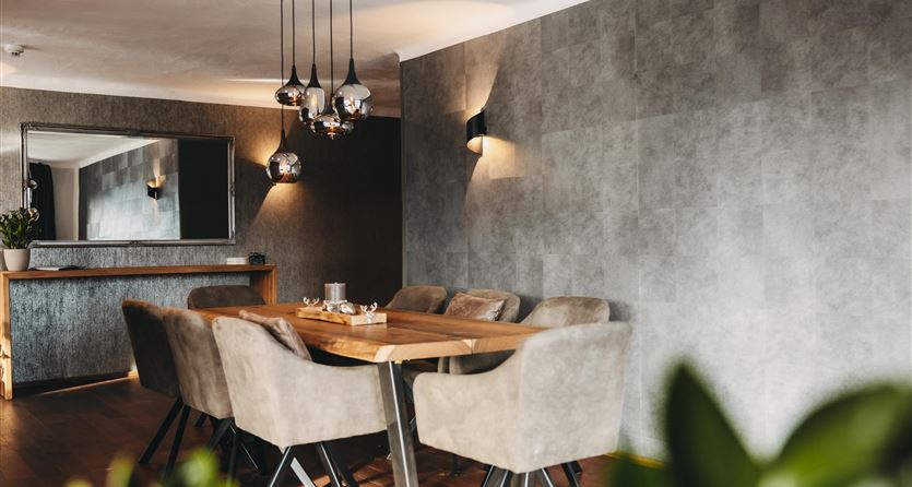 Ein modernes Esszimmer mit einem großen Tisch aus Holz und eleganten Stühlen. Die Wände sind neutral gehalten, und stilvolle Lampen sorgen für angenehmes Licht.