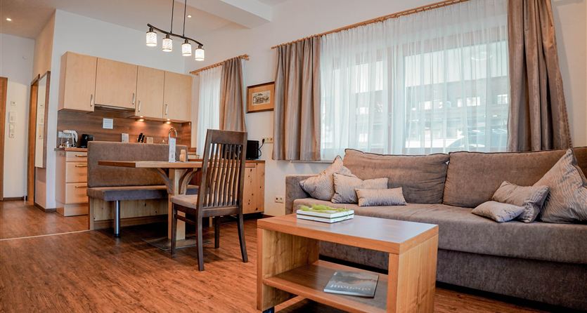 Eine gemütliche Wohnküche mit einem Sofa und einem Holzkaffeetisch. Der Raum ist hell erleuchtet und hat große Fenster.