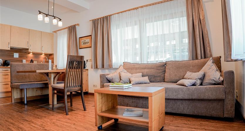 Ein modernes Wohnzimmer mit einem komfortablen Sofa und einem Holztisch. Die großen Fenster sorgen für viel natürliches Licht und Gemütlichkeit.