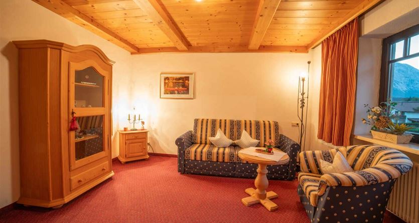 Een gezellige woonkamer met houten balkenplafond, bank en stoelen. Er is een tafel en een kast die veel opbergruimte biedt.