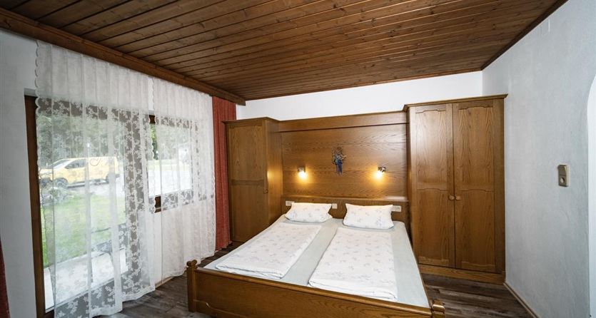 Ein gemütliches Schlafzimmer mit zwei Betten und Holzmöbeln. Das Zimmer hat ein Fenster mit Vorhängen, das Tageslicht hereinlässt.