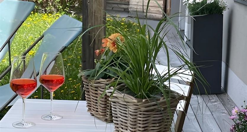 A beautiful table with two glasses on a terrace. In the middle are baskets with plants and the surroundings are friendly and inviting.