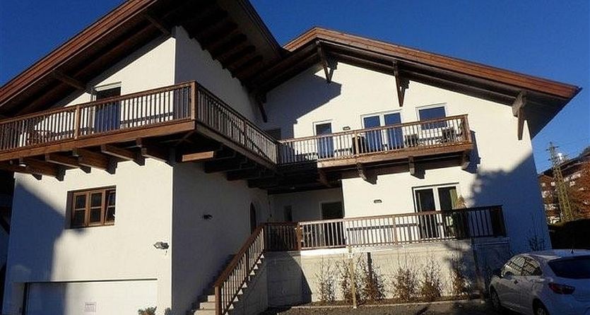 Een modern huis met een lichte buitenverf en een groot balkon. De lucht is helder en blauw.