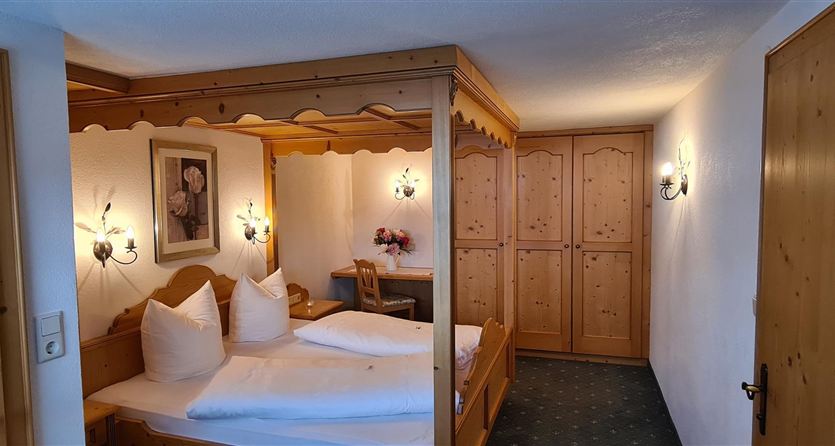 Een gezellige slaapkamer met een houten hemelbed. De ruimte is licht en vriendelijk, met een drijfhoutkast en warme verlichting.