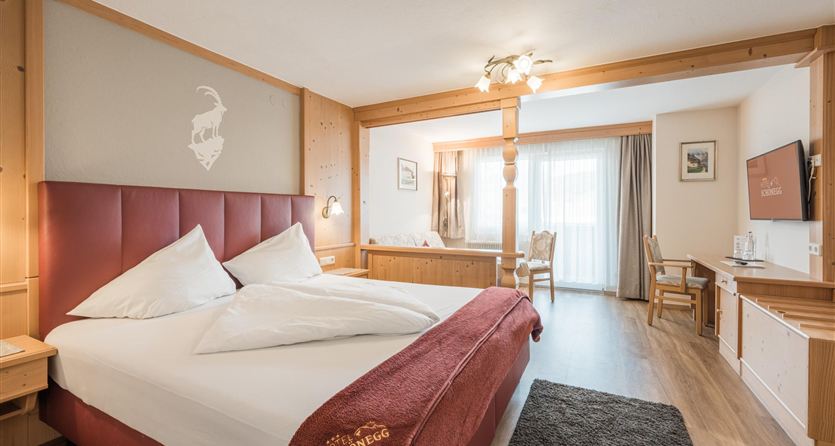 Una camera d'hotel moderna con un grande letto, accenti e un'atmosfera accogliente.  <br/>La stanza è dotata di dettagli in legno e di una finestra con luce naturale, oltre a un balcone.