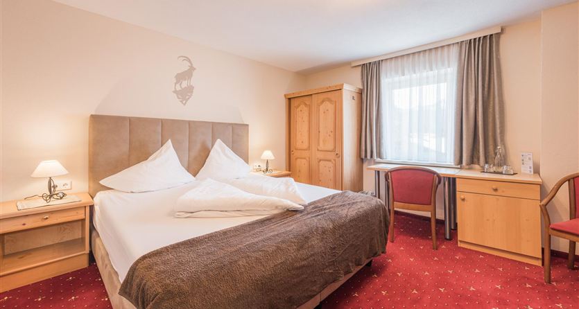 Una camera d'hotel accogliente con un grande letto e un tappeto a motivi rossi. La stanza è luminosa e ben arredata, con una scrivania e una finestra.