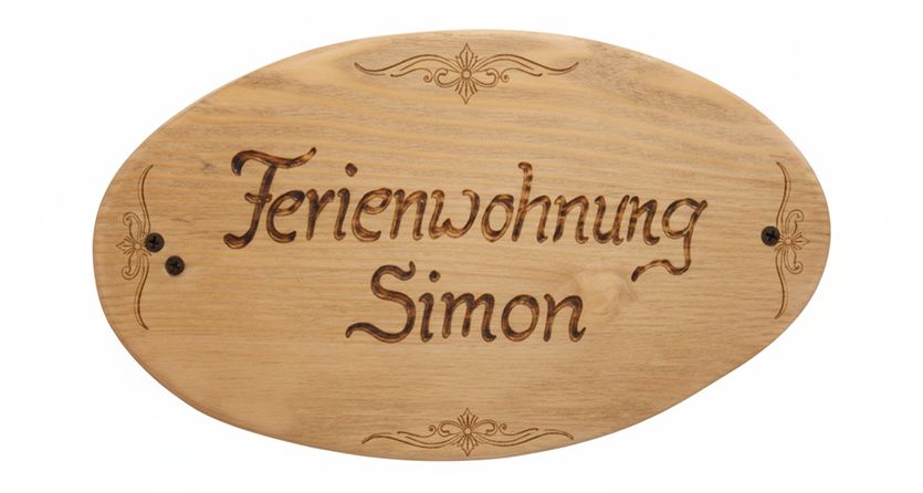 Ein Holzschild mit der Aufschrift "Ferienwohnung Simon". Es hat eine ovale Form und dekorative Verzierungen.
