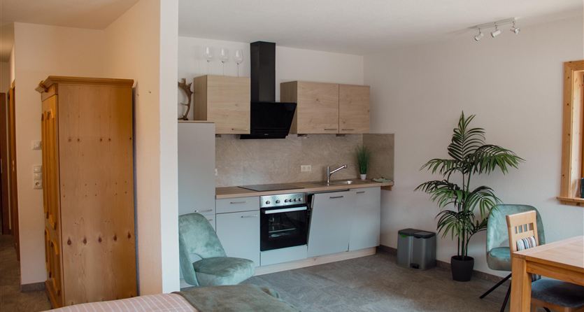 A modernliving kitchen with a bed and a table. In the background, some plants and a well-equipped kitchen corner can be seen.