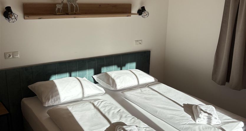 Een lichte slaapkamer met twee eenpersoonsbedden en frisse handdoeken. De muren zijn neutraal, en er is een gezellige houten plafond.