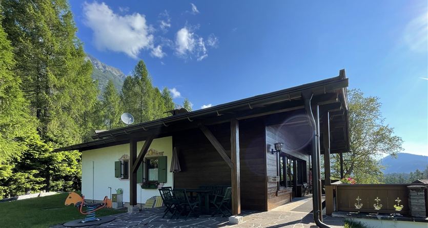 Ein charmantes Holzhaus umgeben von Bäumen und einer schönen Landschaft. Der Himmel ist klar und die Atmosphäre ist ruhig und einladend.
