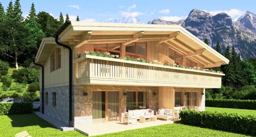 Una casa in legno moderna in montagna con un elegante balcone. È circondata da un prato verde e alberi, creando un'atmosfera idilliaca.