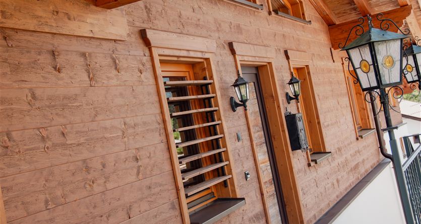 A rustic wooden facade with windows and lamps. The entrance displays traditional, artisanal style.