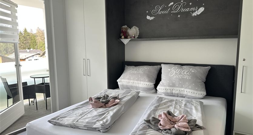 A modern bedroom with a double bed and elegant pillows. Large windows provide a view outside and ensure bright lighting.