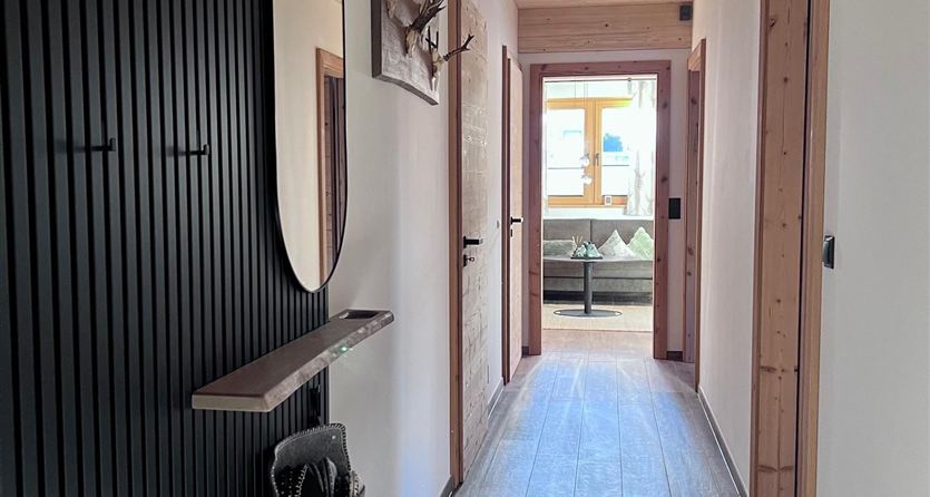 Ein heller Flur mit Holzdecke und modernen Wänden. Auf der linken Seite befindet sich ein runder Spiegel und eine Garderobe.