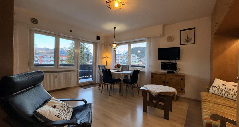 Ein helle und gemütliche Wohnräume mit einem Sofa und einem Esstisch. Große Fenster sorgen für viel Tageslicht.