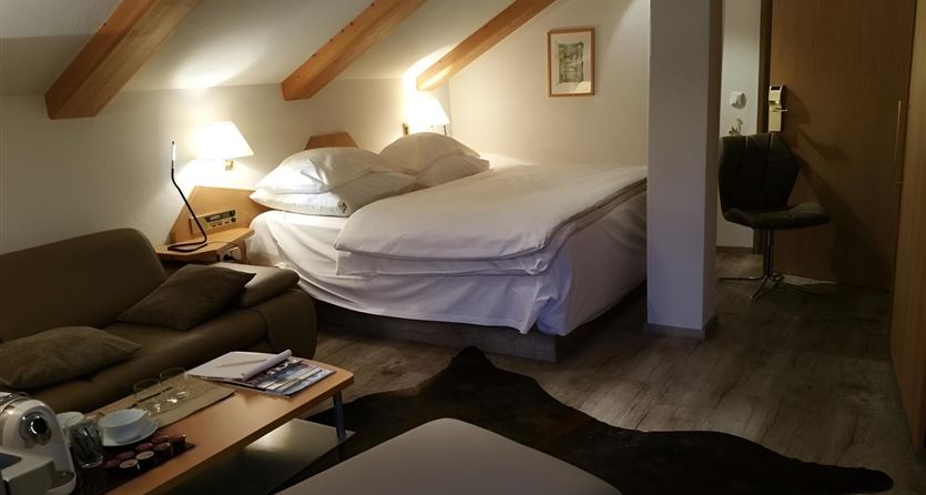 Ein gemütliches Hotelzimmer mit einem großen Bett, einer Couch und einem Tisch. Es gibt Holzdecken und sanfte Beleuchtung.