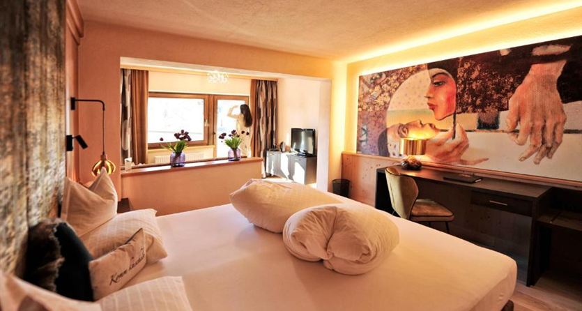 Ein modernes Hotelzimmer mit einem großen Bett und stilvollen Möbeln. An der Wand hängt ein künstlerisches Gemälde, das das Zimmer dekoriert.