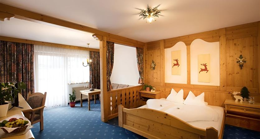 Ein gemütliches Hotelzimmer mit Holzverkleidung und einem großen Bett. Die Fenster bieten viel Tageslicht und die Dekoration ist rustikal und einladend.