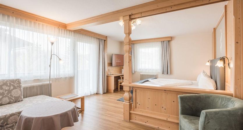 A cozy room with wood paneling and a large window. There is a living area with a table and chairs as well as a bedroom with a double bed.