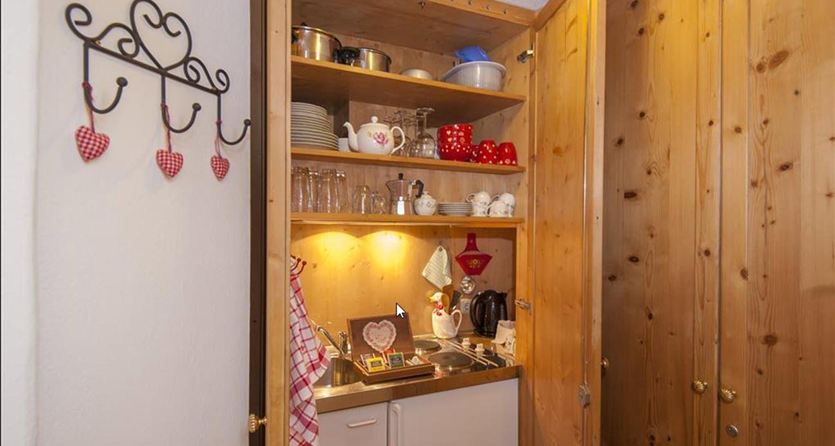 Een mooie houten keukenkast met servies en glazen. De binnenruimte is goed verlicht en toont enkele decoratieve elementen.