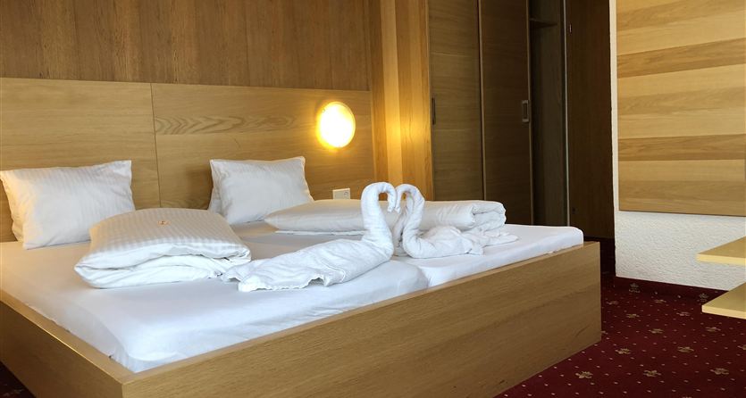 Een moderne slaapkamer met een groot tweepersoonsbed en houten wandbekleding. Op het bed liggen kunstzinnig gevormde handdoeken in de vorm van zwanen.