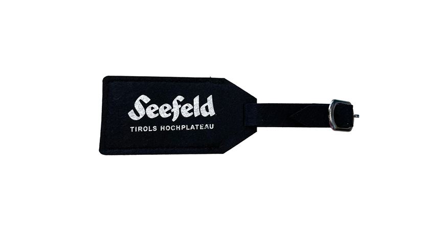 Ein schwarzes Gepäckanhänger mit dem Schriftzug "Seefeld Tirols Hochplateau". Ideal für Reisende, die nach Seefeld kommen möchten.