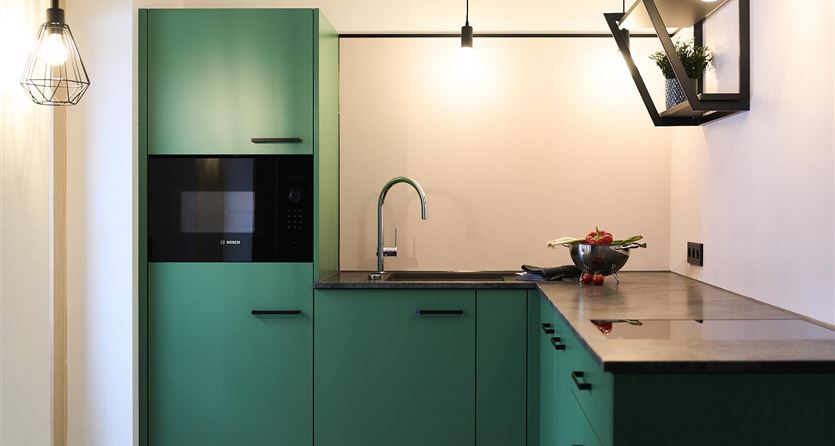 Eine moderne Küche mit grünen Schränken und einer schwarzen Arbeitsplatte. Die Einrichtung ist schlicht und elegant, mit gutem Licht von stilvollen Lampen.