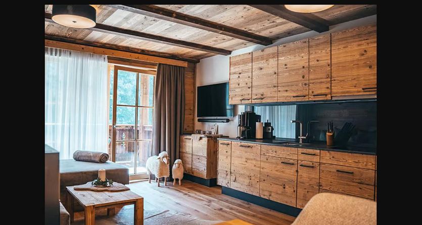 Een moderne woonkamer met houten planken en een goed uitgeruste keuken. Grote ramen laten veel licht binnen en bieden toegang tot een balkon.