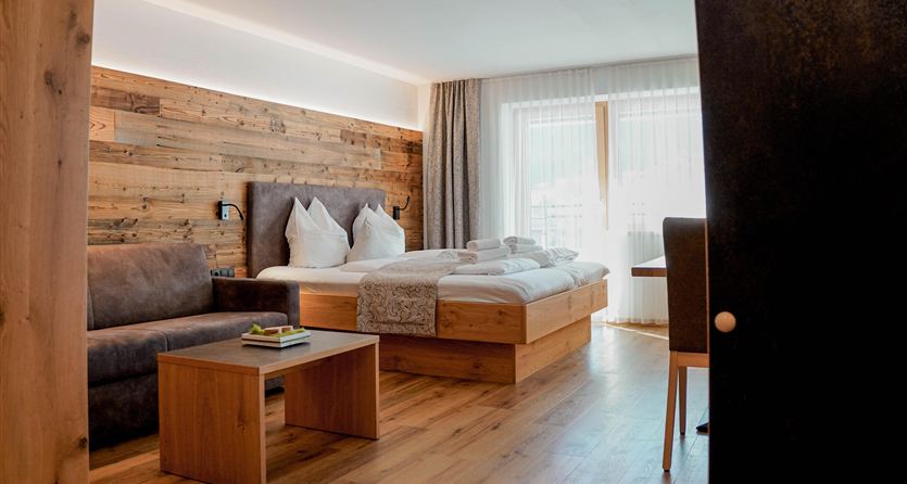Ein modernes Hotelzimmer mit Holzwänden und einem gemütlichen Bett. Große Fenster sorgen für viel natürliches Licht.