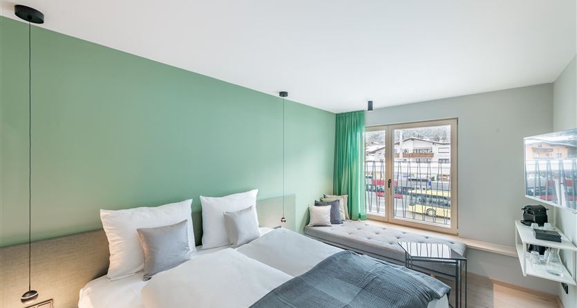 Ein modernes Schlafzimmer mit zwei Betten und einer grünen Wand. Der Raum verfügt über ein Fenster mit Ausblick und stilvollem Mobiliar.