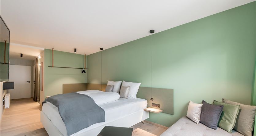 Ein modernes Zimmer mit grünem Wanddesign. Es enthält ein Bett, eine Couch und stilvolle Möbel.