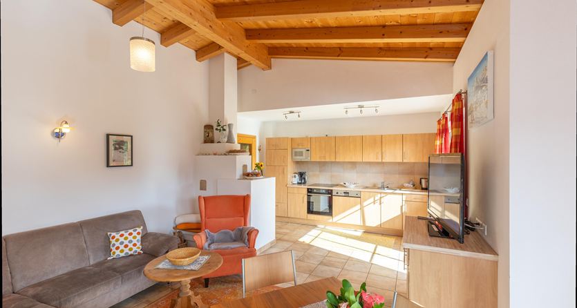 Ein helles Wohnzimmer mit Holzdecken und moderner Küche. Die Möbel sind gemütlich und einladend, ideal für Entspannung.