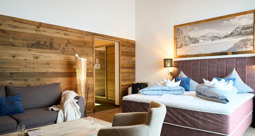 A cozy room with wooden walls and a large double bed. There is a modern seating area with a couch and a table.
