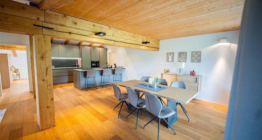 Een modern ingerichte eetruimte met een houten tafel en elegante stoelen. De ruimte heeft grote ramen die veel licht binnenlaten.