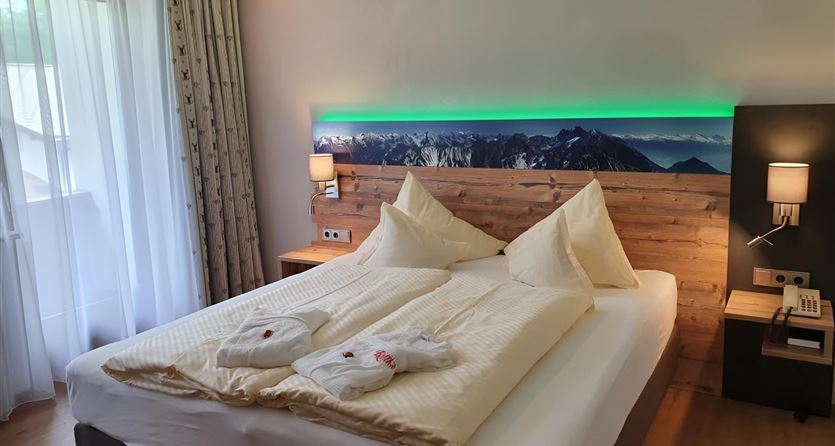 Ein gemütliches Schlafzimmer mit einem großen Bett und sanften Lichtakzenten. Die Wände sind in warmen Farben gehalten, und es gibt eine Fensterfront, die viel Tageslicht hereinlässt.