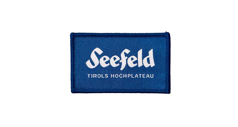 Ein blauer Aufnäher mit dem Schriftzug "Seefeld" und der Unterzeile "Tirols Hochplateau". Das Design vermittelt eine alpine Atmosphäre.