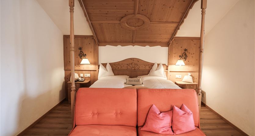 Ein gemütliches Schlafzimmer mit einem Himmelbett und einem orangefarbenen Sofa. Die Wände sind in warmen Tönen gehalten und schaffen eine einladende Atmosphäre.