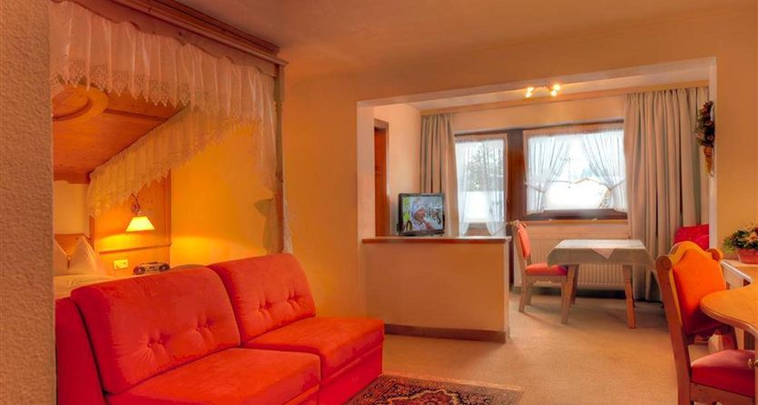 Ein gemütliches Wohnzimmer mit einem roten Sofa und einem Esstisch. Große Fenster sorgen für viel Licht im Raum.