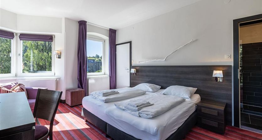 A modern hotel room with two single beds and a table. Large windows provide plenty of daylight and a pleasant atmosphere.