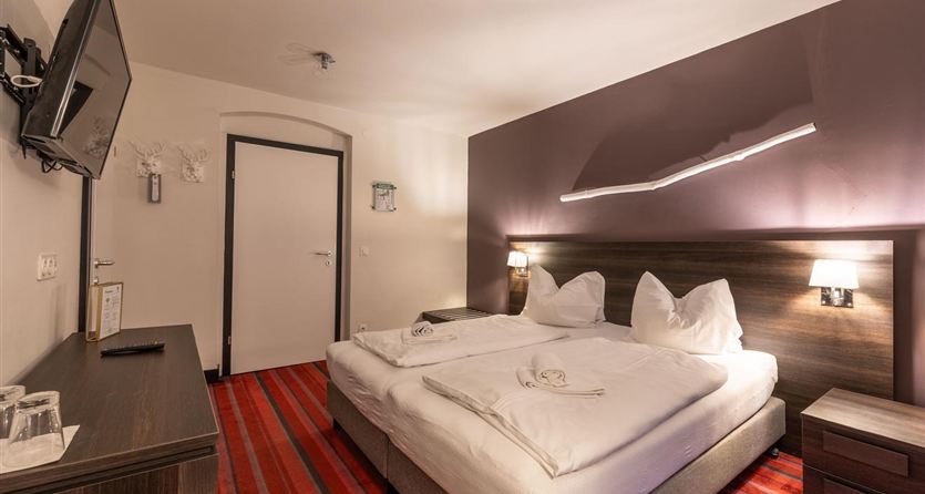 A modern bedroom with a large bed and bright bedding. The walls are in soft colors and there is a television on the wall.