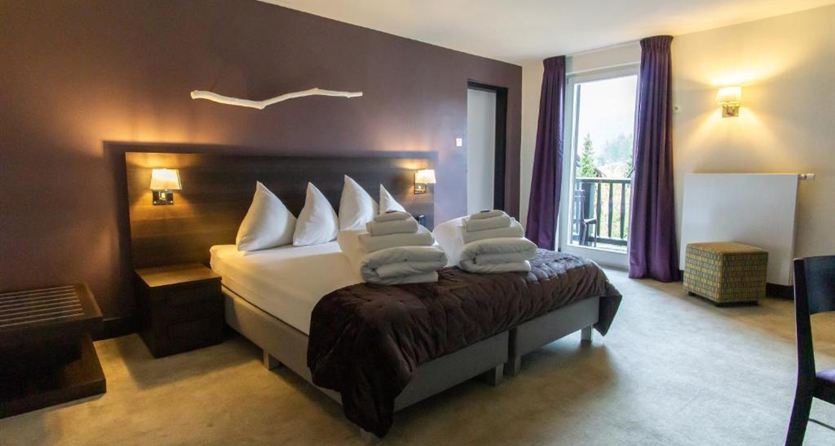 A modern hotel room with a double bed and fresh towels. Large windows provide plenty of light and a view of the balcony.
