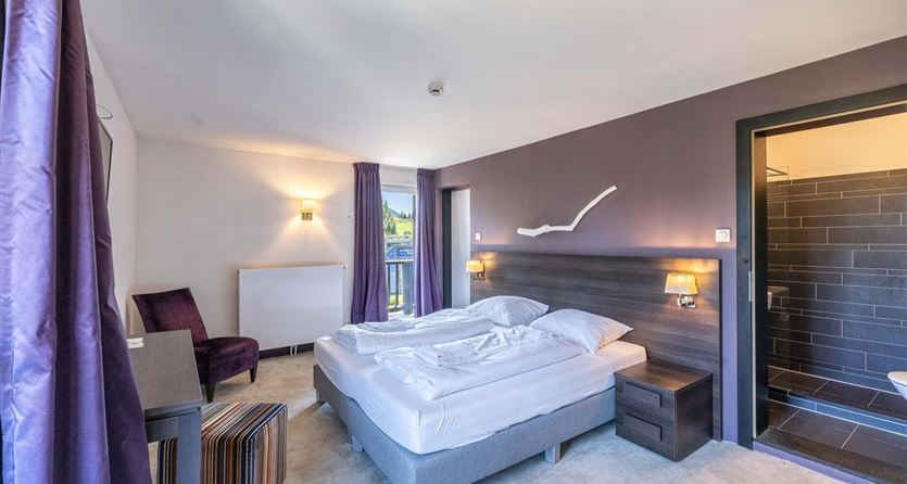 A modern hotel room with a double bed and cozy furnishings. The walls are in soft colors and there is pleasant lighting.