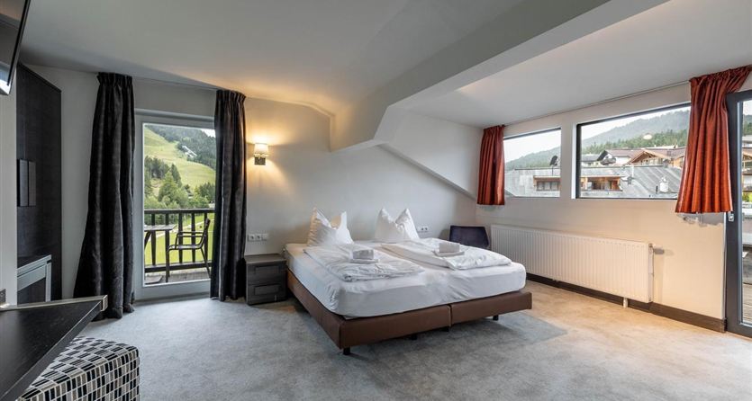 A modern room with a double bed and large windows that offer a view of the mountains. The room is bright and tastefully furnished.