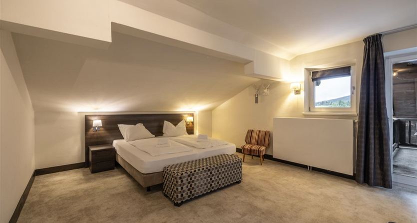 A modern bedroom with a large bed and a cozy armchair. The room has a bright atmosphere and a window with a view outside.