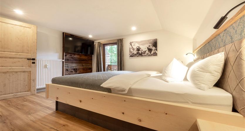 Een moderne slaapkamer met een groot bed en veel kussens. De kamer heeft een houten vloer en gezellige verlichting.