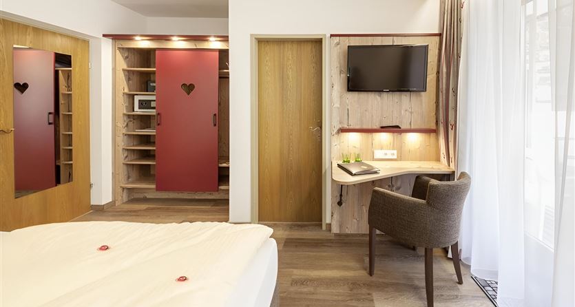 Ein gemütliches Hotelzimmer mit einem großen Bett, einem Fernseher und einem Schreibtisch. Die warmen Farben und das Holzdesign schaffen eine einladende Atmosphäre.